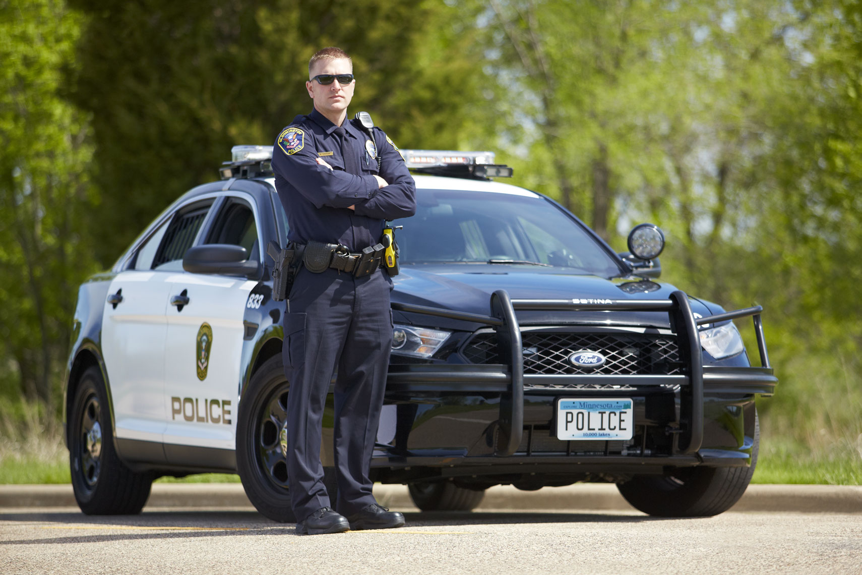 Confident cop/standing/front of cop car/trees/lifestyle photography